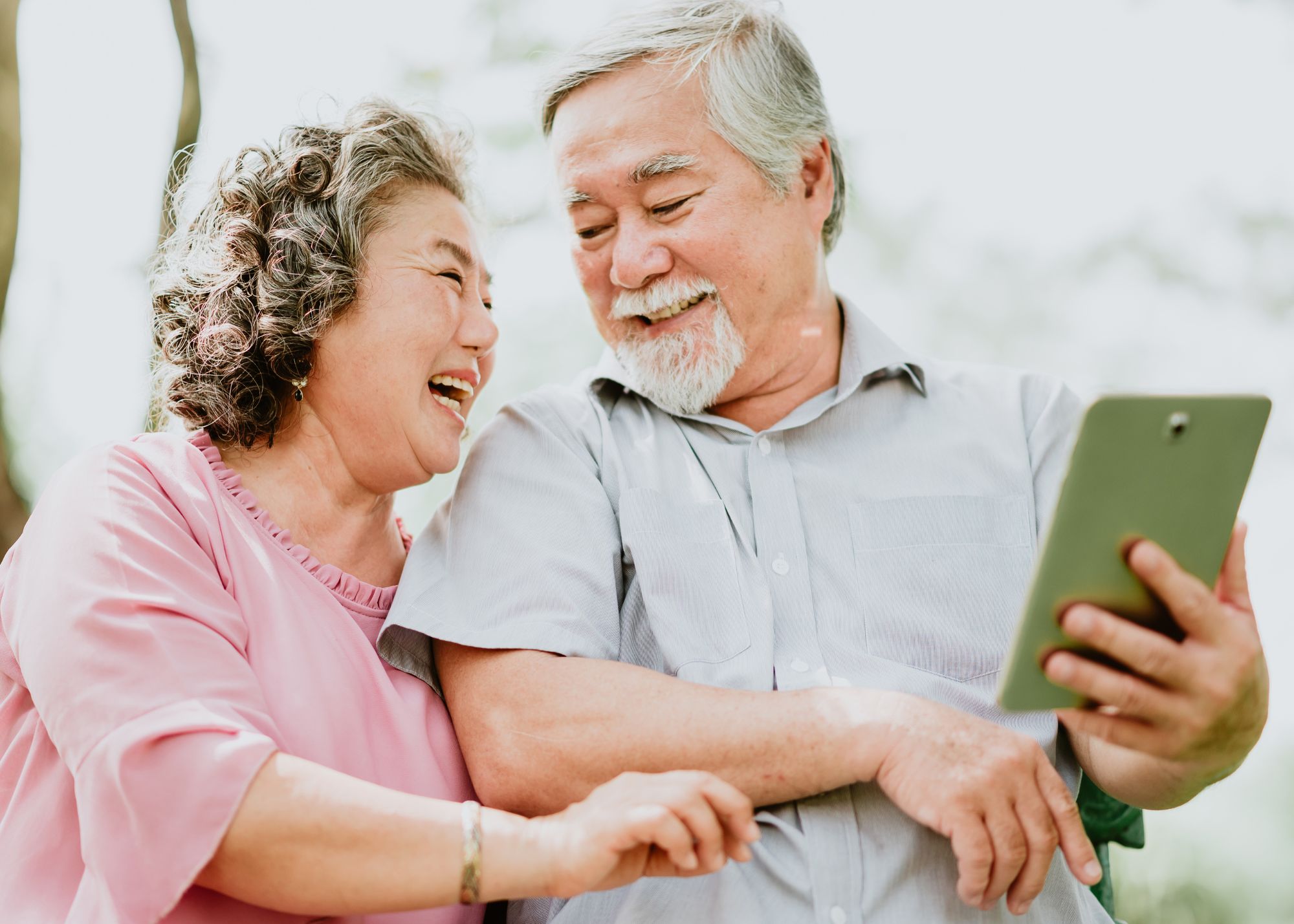 Elderly Asian Man and Woman Looking at tablet and laughing and smiling - Warren Real Estate Senior's Resources Page